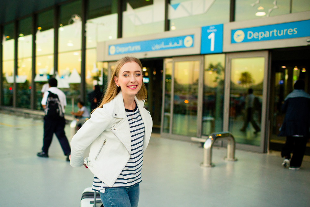 girl-white-jacket-stripped-shirt-walks-with-suitcase-from-airport